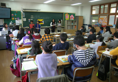 Photo of a school room filled with middle-grade children facing the blackboard away from the camera