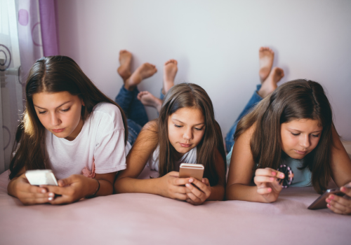 Photo of 3 middle school-aged girls lying on the floor next to each other looking at their phones