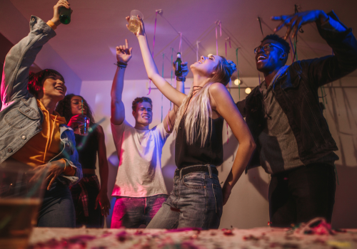 Photo of high schoolers dancing and raising glasses in a room with streamers