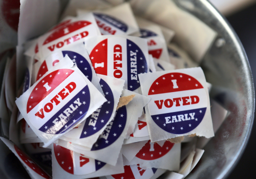 Photo of a silver bucket holding red, white & blue stickers, "I Voted Early"