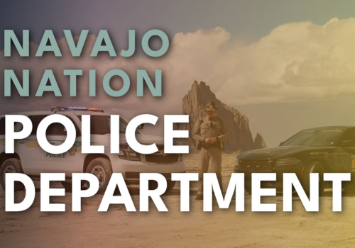 Image of a police officer standing between to police cars w/a large rock formation in the background