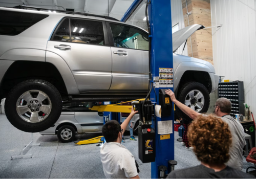 Several people face a silver SUV about head high on a lift as the teacher presses a button