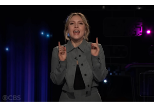 A young, blonde woman in a gray suit gestures