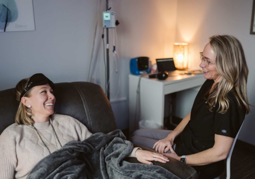 A woman patient covered by a blanket on a sofa smiles at a woman technician sitting next to her