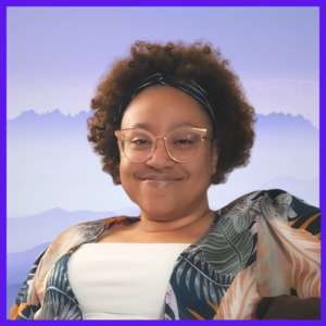 A smiling Black woman with curly, brown hair and wearing glasses